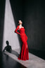 Woman in a red evening gown standing against a dark background with spotlight effect
