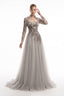 A floor-length formal gown with long sheer sleeves, a Queen Anne neckline, and intricate floral shiny beading embroidery embellishment on the bodice, worn by a model against a plain white studio background.