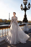 A woman wearing a long-sleeved, floor-length tulle gown with floral embroidery stands on a Parisian bridge with the Eiffel Tower and river in the background.