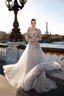 A woman wearing a voluminous gray-colored evening gown with intricate embroidery stands on a Parisian bridge with the Eiffel Tower and river in the background.